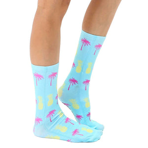 A pair of blue socks with a pattern of pink palm trees and yellow pineapples.