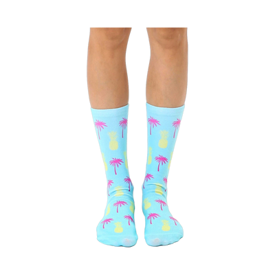 Pair of light blue crew socks with a fun, repeating pattern of pink palm trees and yellow pineapples.