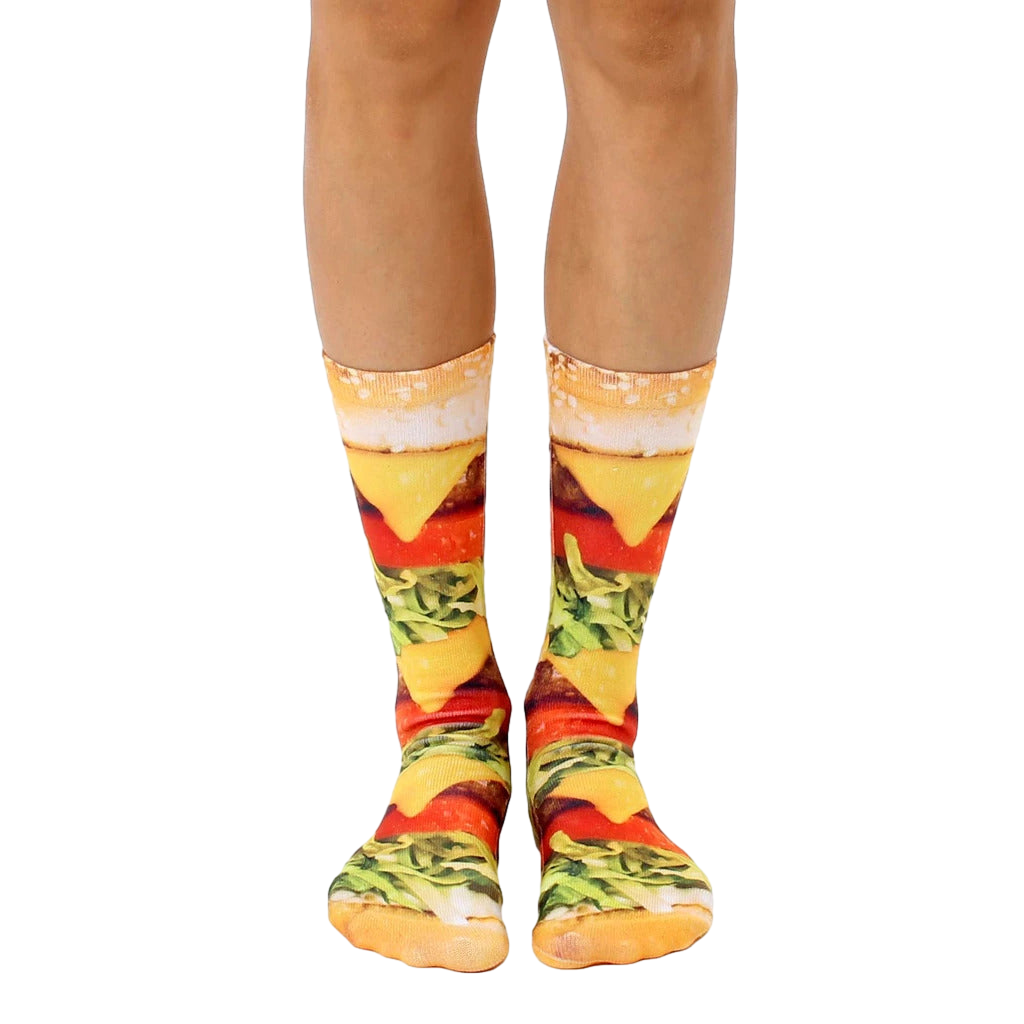 A pair of crew socks with a realistic burger print.  The main colors are yellow, red, green, and brown. [lf]