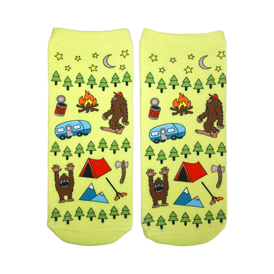 A pair of lime green ankle socks with a fun camping design. The pattern includes Bigfoot, a camper, tent, trees, and stars.