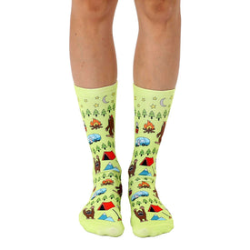 green crew socks featuring bigfoot camping in forests and mountains. images of trees, stars, marshmallows and tent.  
