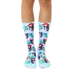 Pair of crew socks in pastel blue, featuring a whimsical pattern of skulls wearing floral crowns and tropical leaves. [lf]