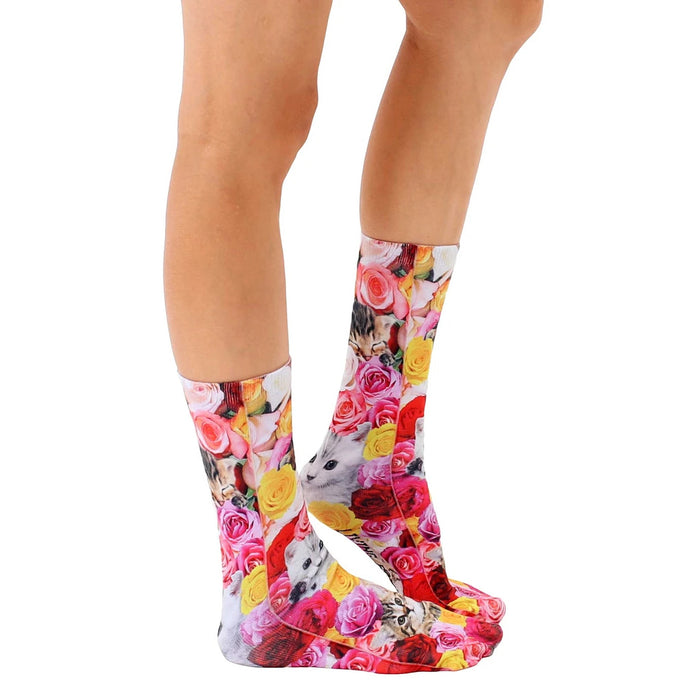 A pair of socks with a repeating pattern of roses and kittens. The socks are white with the pattern printed in pink, red, yellow, and green.