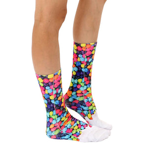 A pair of mid-calf socks with a colorful pattern of round candy pieces on a white background.