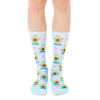 Pair of light blue crew socks with a repeating pattern of cartoon avocados doing yoga poses and pink hearts. [lf]