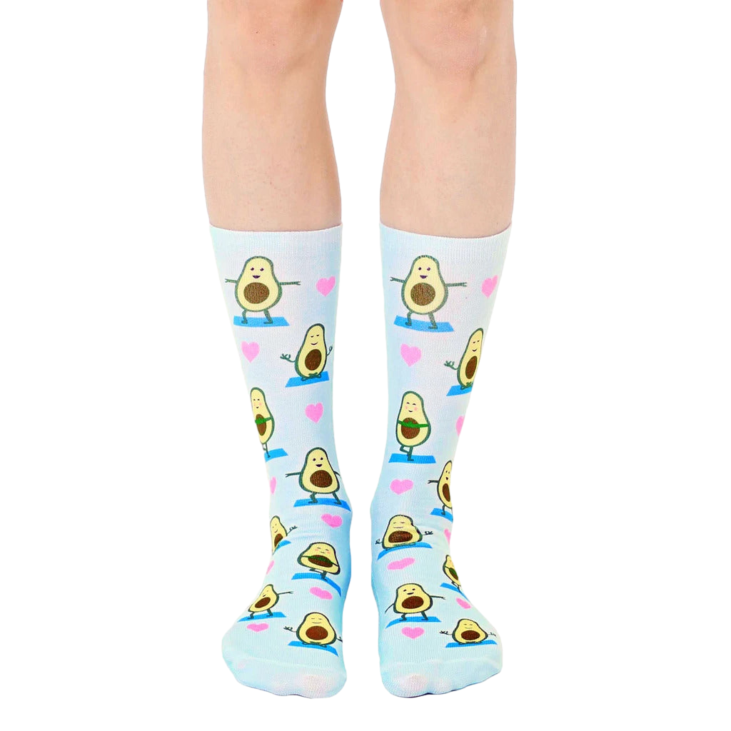 Pair of light blue crew socks with a repeating pattern of cartoon avocados doing yoga poses and pink hearts. [lf]