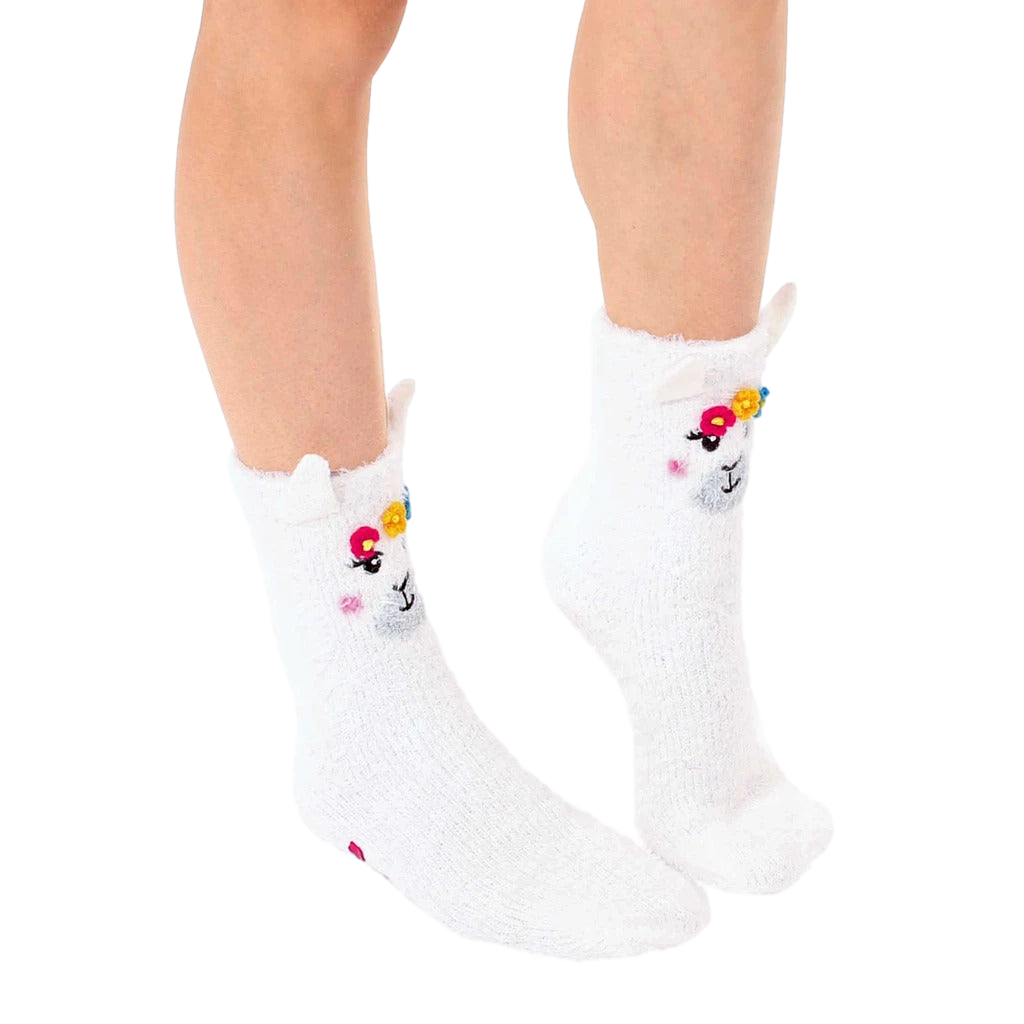 Pair of white fuzzy llama slipper socks.  Features embroidered llama faces with flower crowns and pink non-skid grips. [lf]