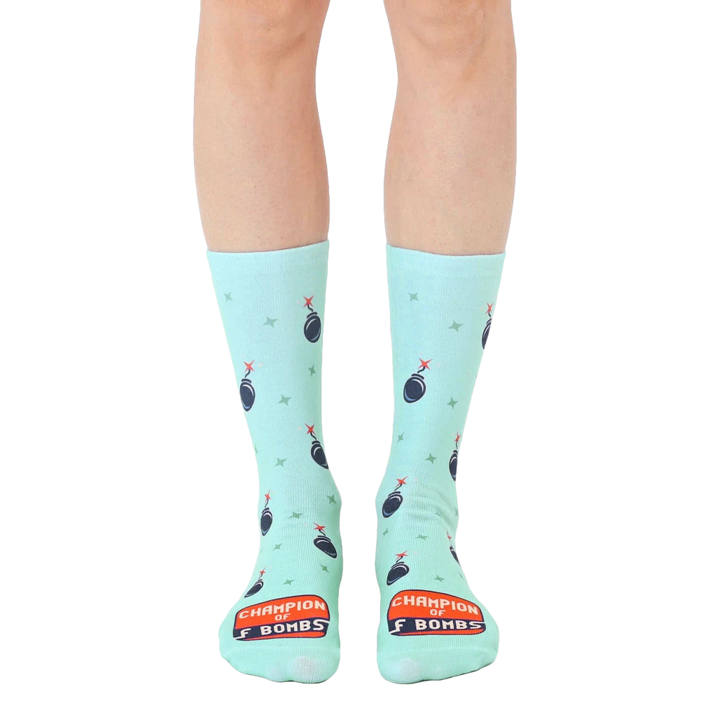A pair of mint green crew socks with a repeating pattern of cartoon bombs and the text 'Champion of F Bombs'. [lf]