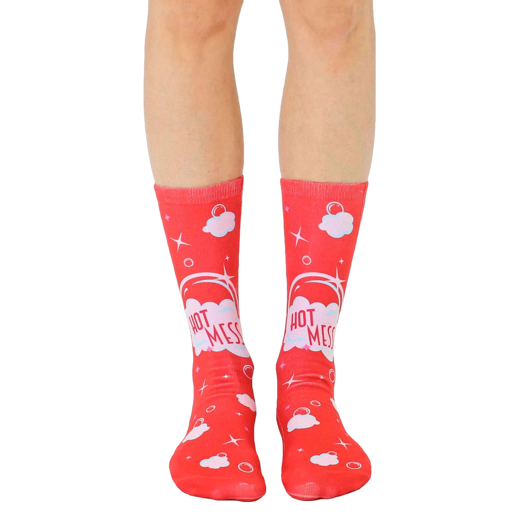 Pair of red crew socks with a playful design.  Features a 'Hot Mess' slogan inside pastel pink speech bubbles, surrounded by clouds and sparkles. [lf]