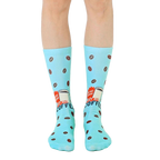 Pair of light blue crew socks with a retro coffee cup design and scattered coffee beans.  'Instant Human' text is visible. [lf]