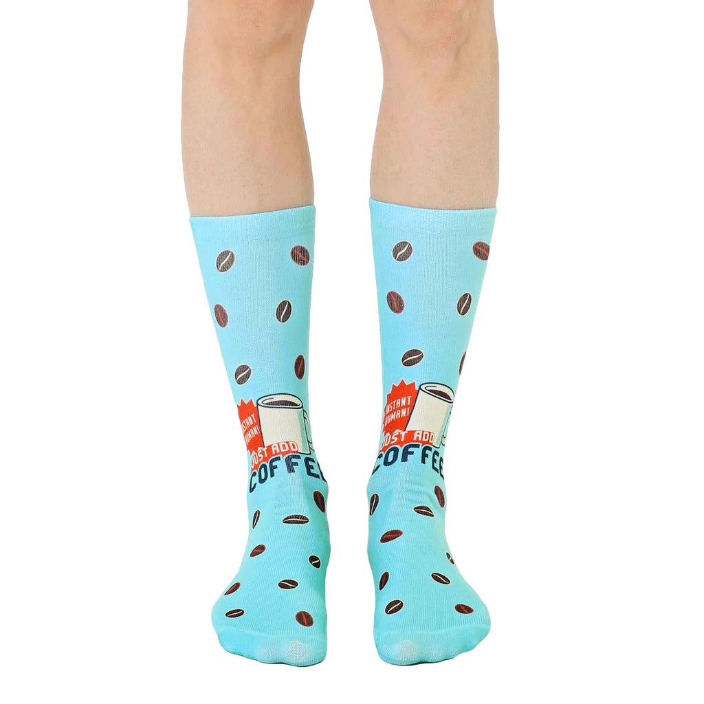 Pair of light blue crew socks with a retro coffee cup design and scattered coffee beans.  'Instant Human' text is visible. [lf]