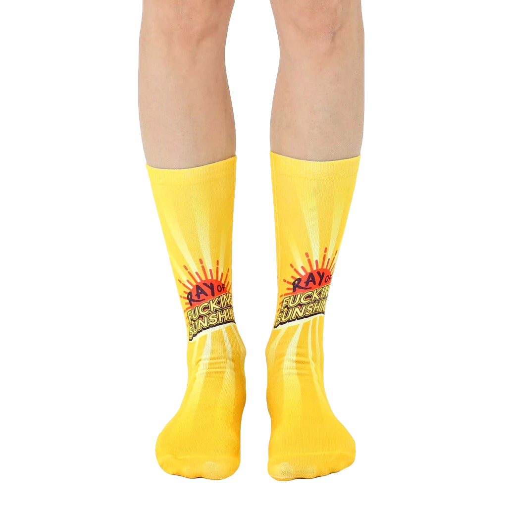 A pair of yellow crew socks with a graphic of a sun and the phrase 'Ray of Fucking Sunshine'. [lf]