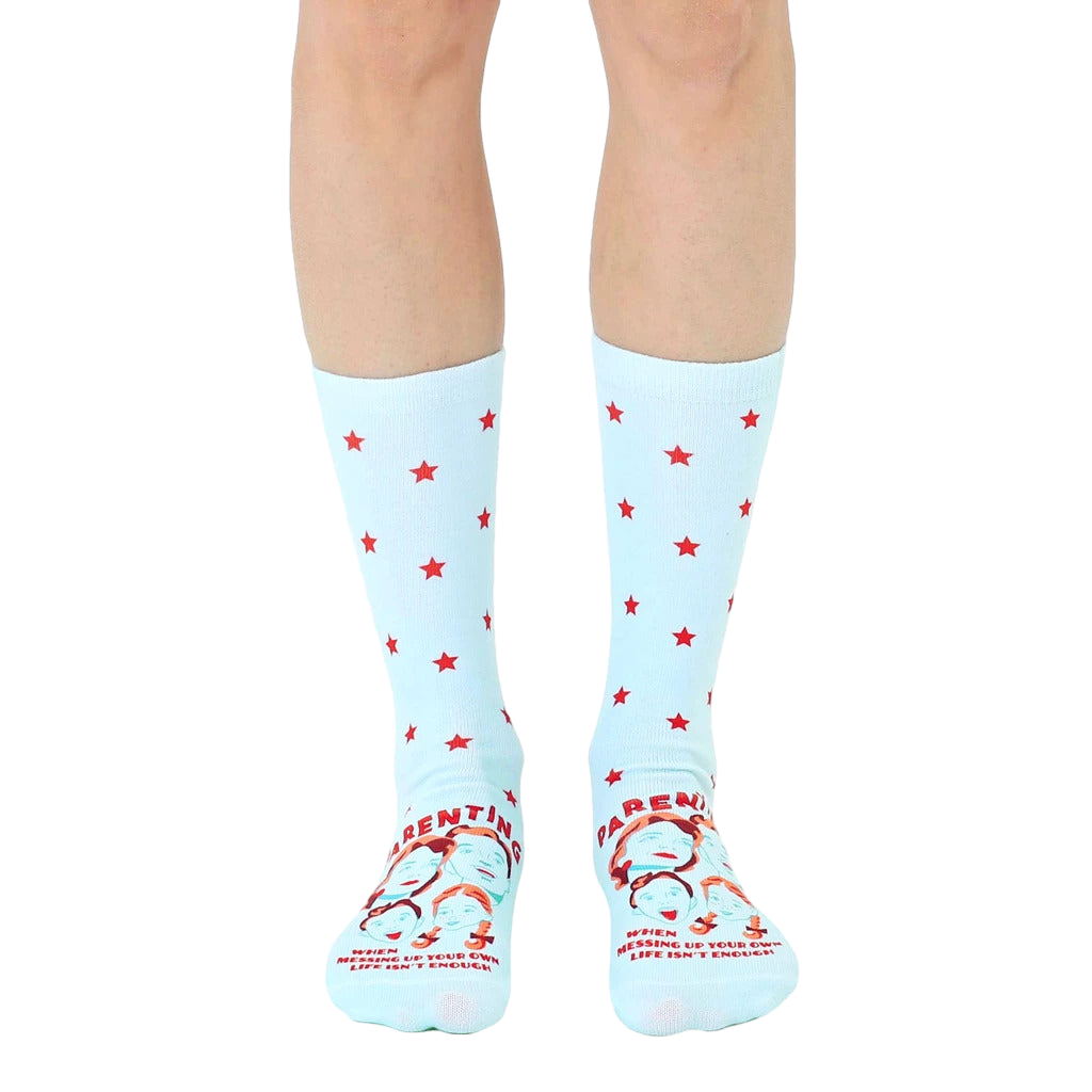 A pair of light blue crew socks with red stars and a humorous parenting quote featuring illustrated faces at the bottom. [lf]