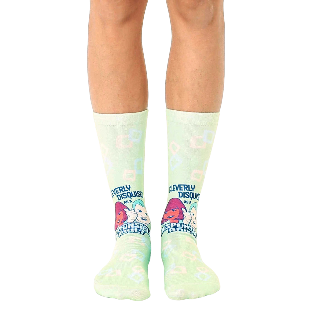 Pair of light green crew socks with a retro design featuring cartoon characters and the text 'Cleverly Disguised as a Responsible Adult'. [lf]