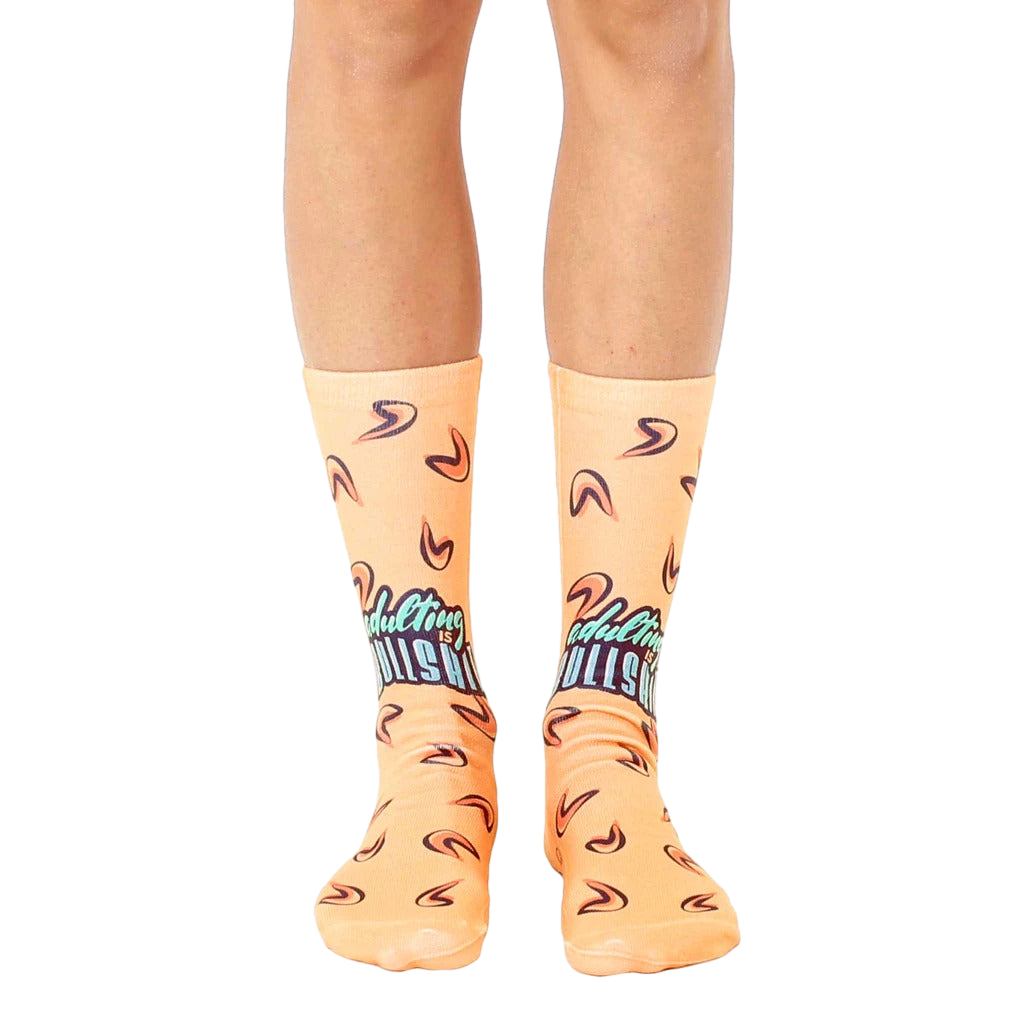 A pair of peach-colored crew socks with a teal 'Adulting is BS' graphic and small fortune cookie designs. Fun and comfy! [lf]
