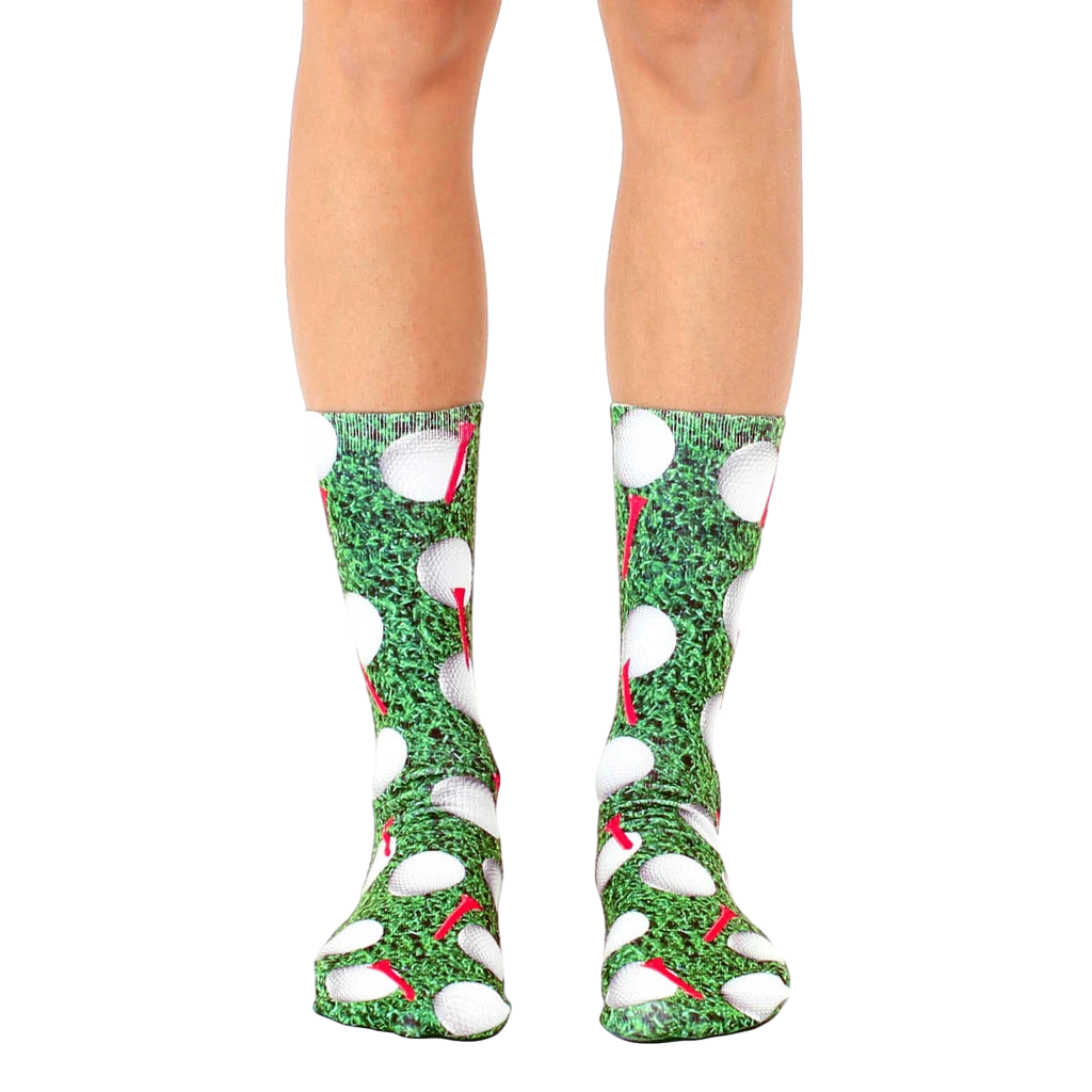 A pair of crew golf socks with a playful design.  The socks are mainly green with white golf balls and red tees. [lf]