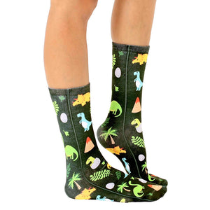 A pair of black socks with a repeating pattern of colorful dinosaurs, dinosaur eggs, volcanoes, palm trees, and leaves.