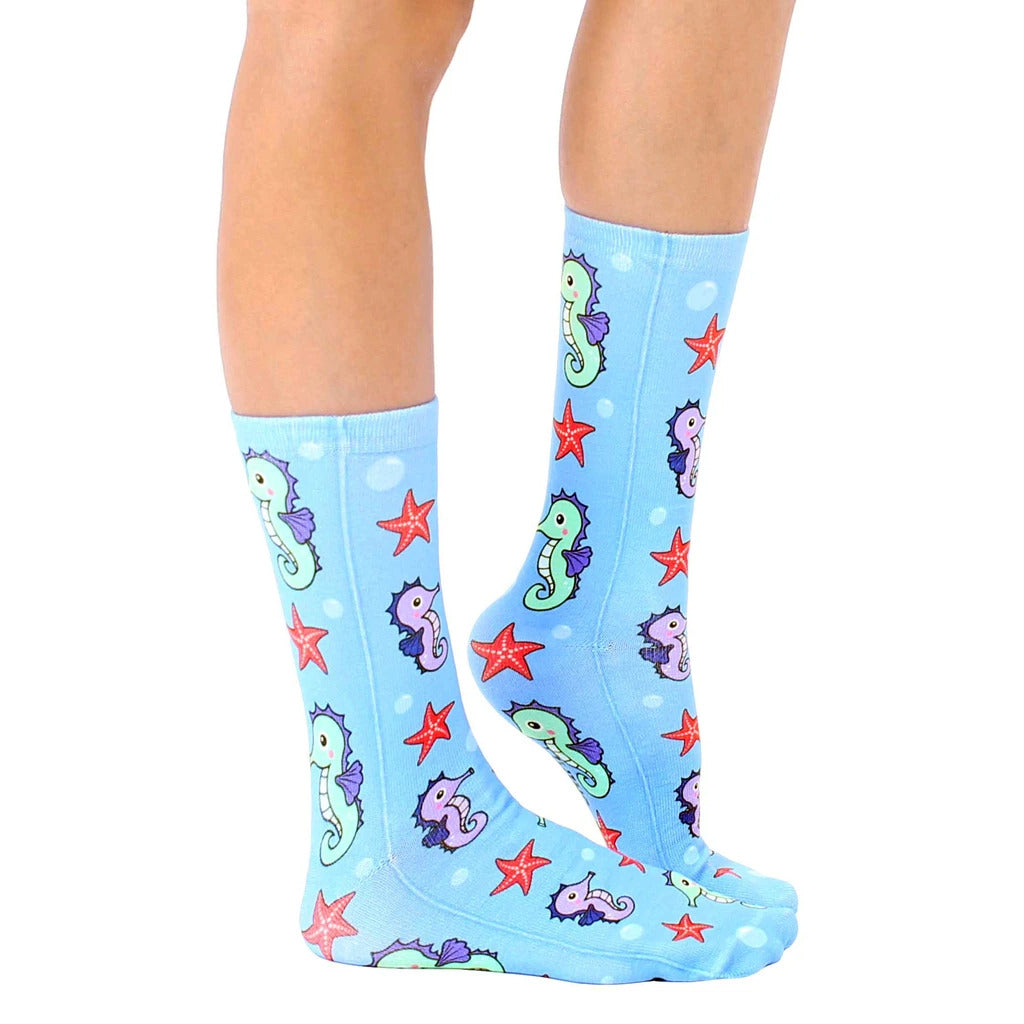 Lifestyle shot: A person's legs showcasing the Seahorse socks.  The socks are predominantly light blue with seahorse and starfish patterns. [lf]