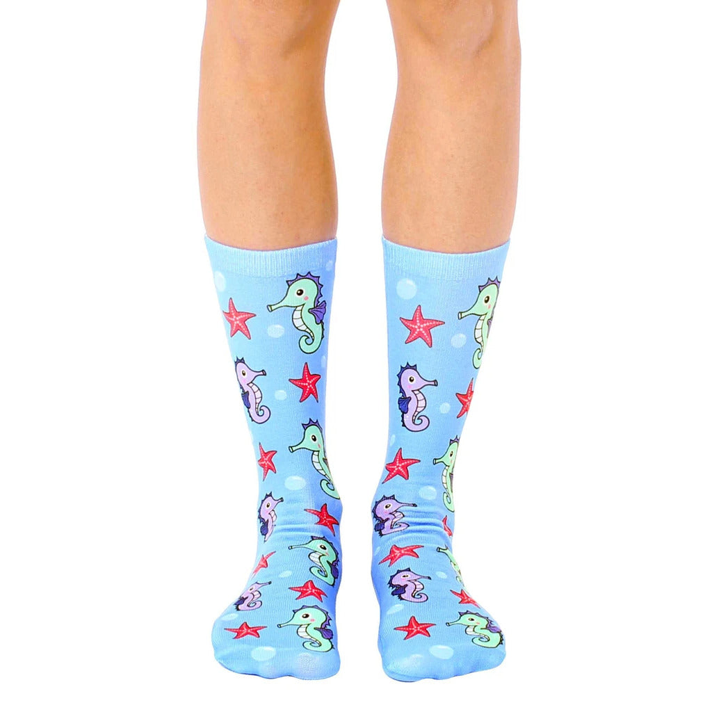A pair of light blue crew socks featuring a pattern of cute seahorses and red starfish. [lf]