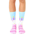 A pair of crew socks showing a birthday cake design.  The socks are light blue, pink, and purple with sprinkles and candles. [lf]