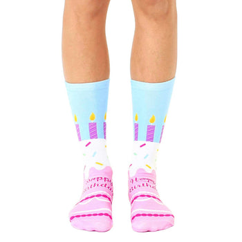 blue socks with white toe and heel. features a repeating pattern of pink and purple birthday cakes with lit candles against a blue background. crew length, made for women. 
