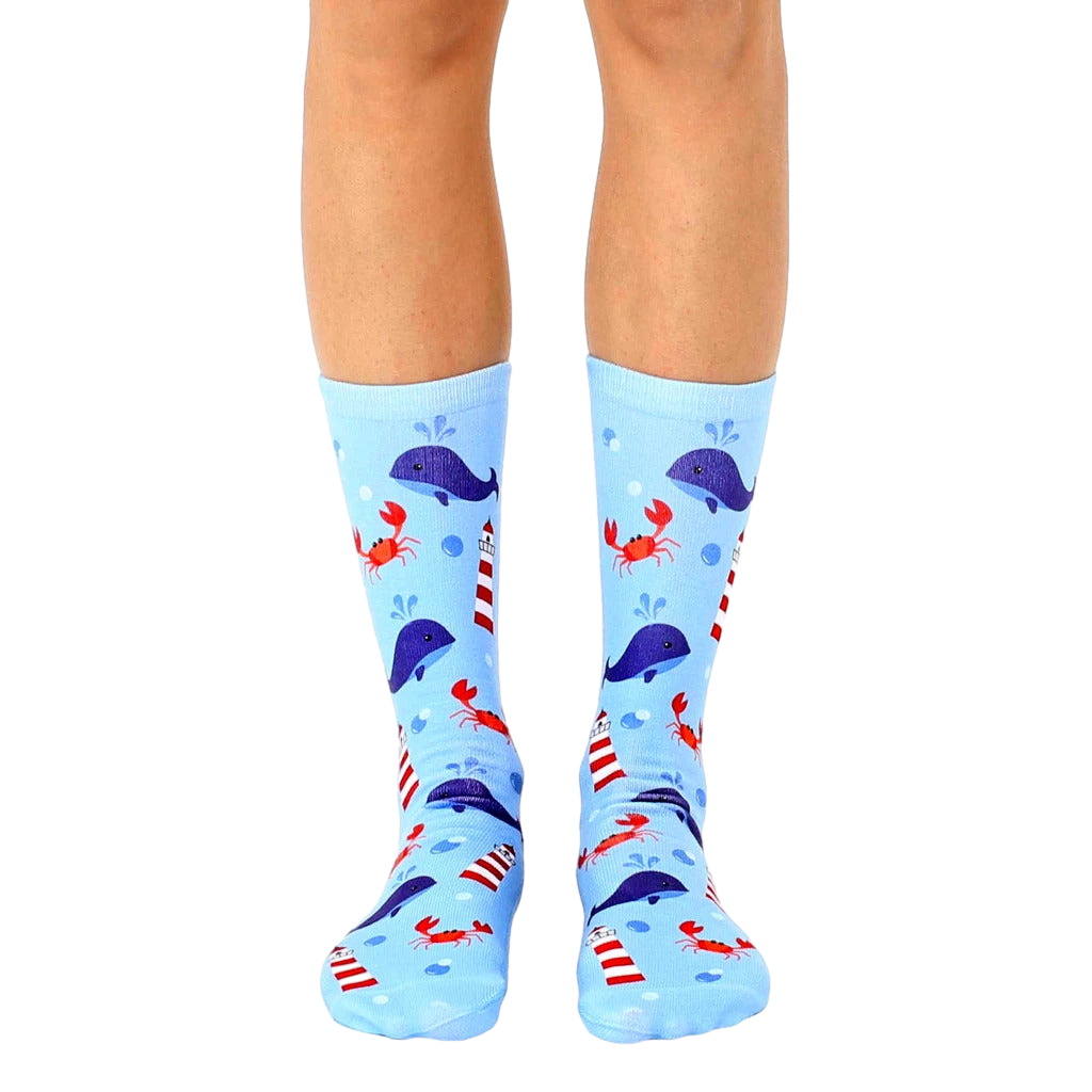 A pair of light blue crew socks with a whimsical design featuring whales, lighthouses, and crabs. [lf]