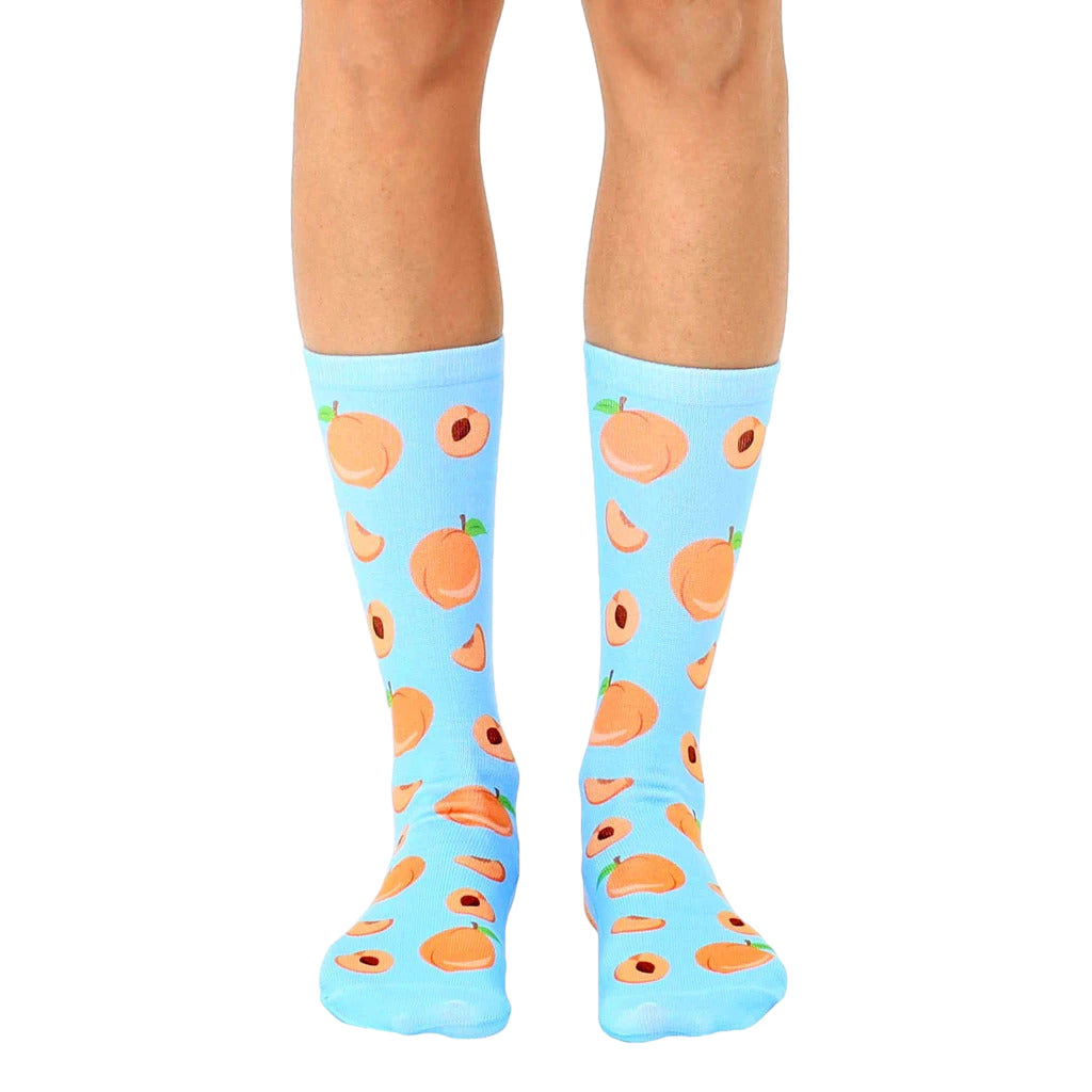 Pair of light blue crew socks with an all-over print of peaches and peach slices. [lf]