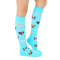 Lifestyle shot of a person wearing the light blue knee-high socks with a pattern of cartoon dogs. The socks extend to the knees and are visible from the mid-calf down. [lf]