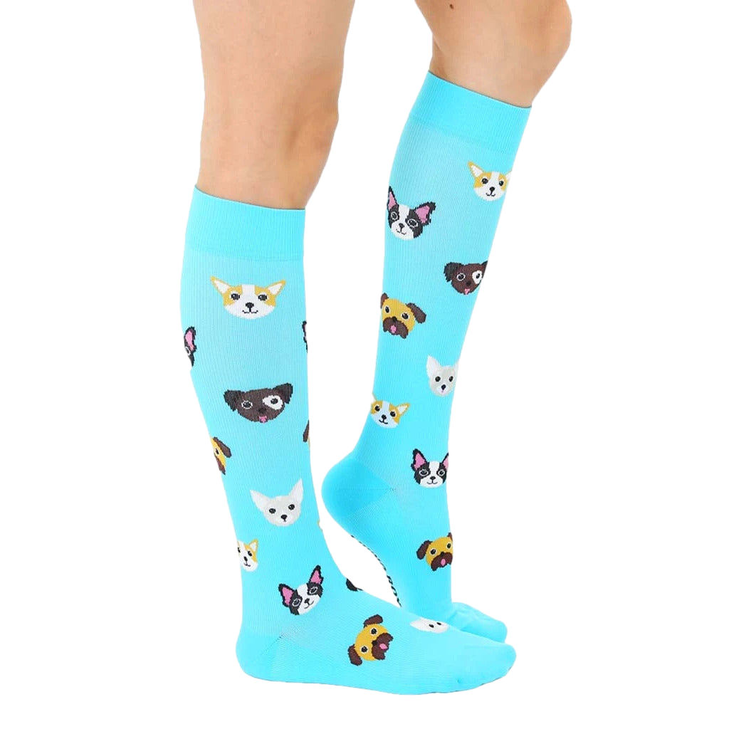 Lifestyle shot of a person wearing the light blue knee-high socks with a pattern of cartoon dogs. The socks extend to the knees and are visible from the mid-calf down. [lf]