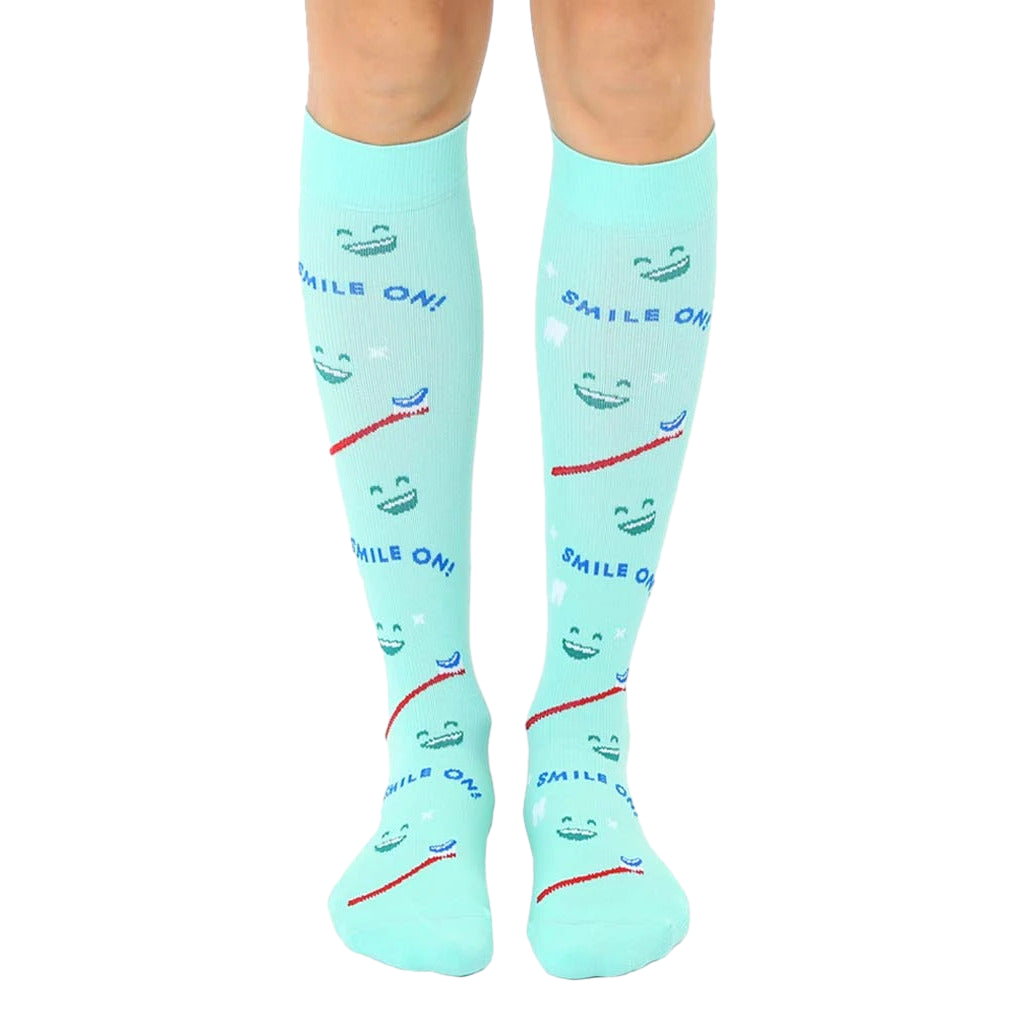 Pair of mint green knee-high socks featuring smiling faces, toothbrushes, and the text 'Smile On!' [lf]