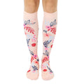 Pair of blush pink knee-high socks with a scattered floral pattern in pink, blue, and red.  Flowers and leaves are illustrated in a painterly style. [lf]