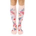 Pair of blush pink knee-high socks with a scattered floral pattern in pink, blue, and red.  Flowers and leaves are illustrated in a painterly style. [lf]
