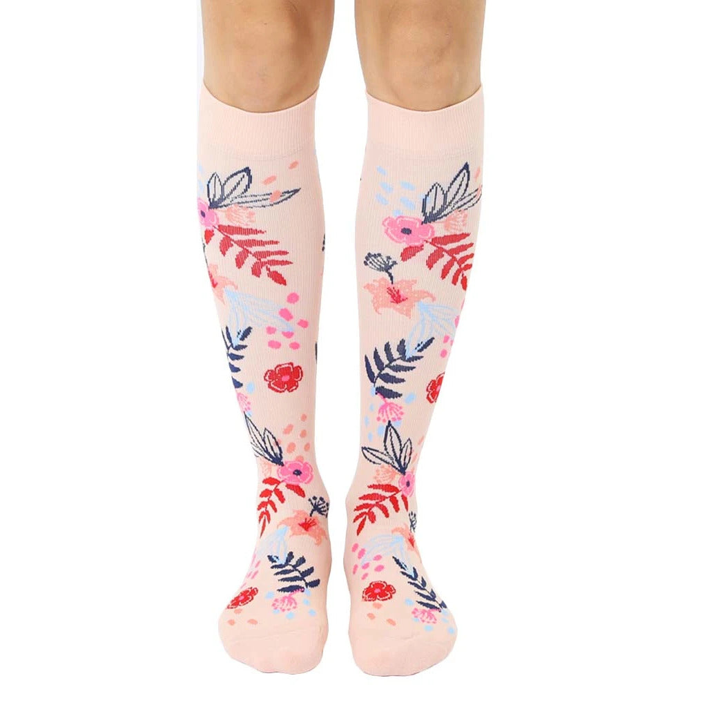 Pair of blush pink knee-high socks with a scattered floral pattern in pink, blue, and red.  Flowers and leaves are illustrated in a painterly style. [lf]