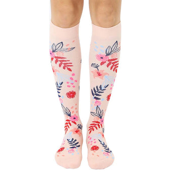 Pair of blush pink knee-high socks with a scattered floral pattern in pink, blue, and red.  Flowers and leaves are illustrated in a painterly style.