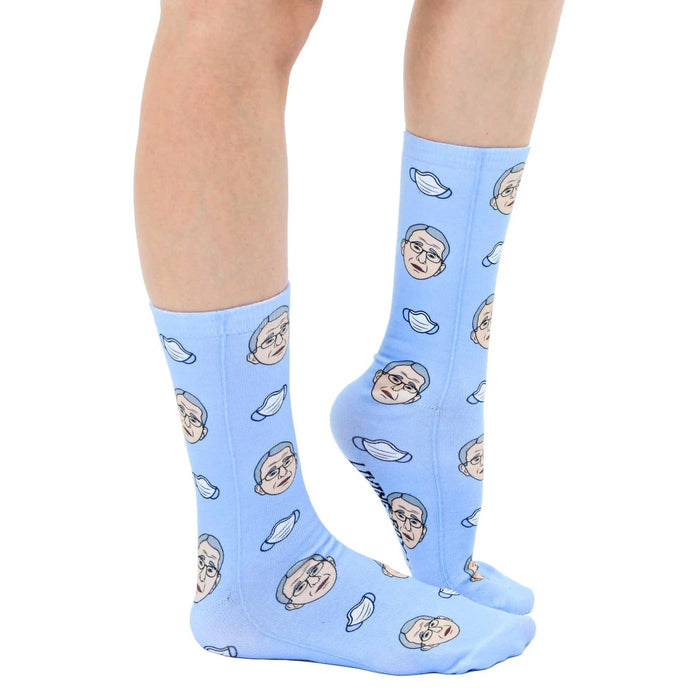A pair of blue socks with a pattern of cartoon Dr. Fauci heads wearing surgical masks.