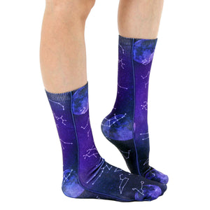 A pair of calf-high socks with a dark blue background and a pattern of white and purple stars and moons.