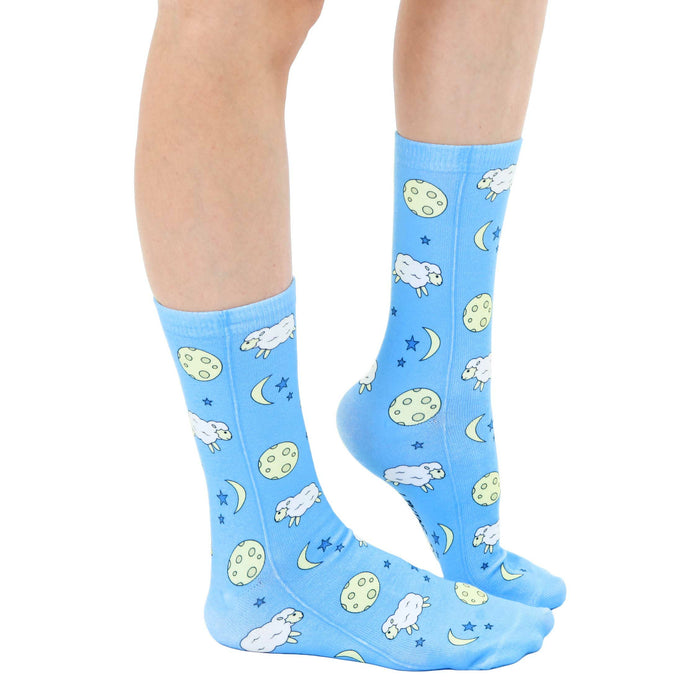 A pair of blue socks with a pattern of white sheep, yellow moons, and stars.