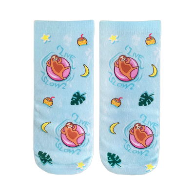 Pair of light blue crew socks.  Design features sloths on pink floaties, tropical fruits, plants, and the text 'Live Slow'.