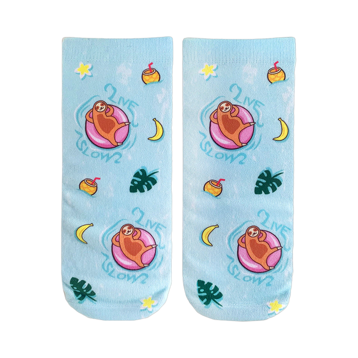 Pair of light blue crew socks.  Design features sloths on pink floaties, tropical fruits, plants, and the text 'Live Slow'. }}