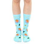 A pair of light blue crew socks with a fun design. Sloths lounging on pink inner tubes in a pool are repeated against a tropical background with yellow stars, moons, and leaves. [lf]