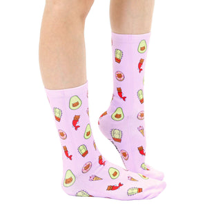 A pair of pink socks with a pattern of cartoon avocados, cacti, donuts, ice cream cones, cats, and mermaids.