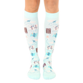 Pair of light blue knee-high socks with a travel theme.  The design includes suitcases, airplanes, maps, and the phrase 'Outta Here'. [lf]