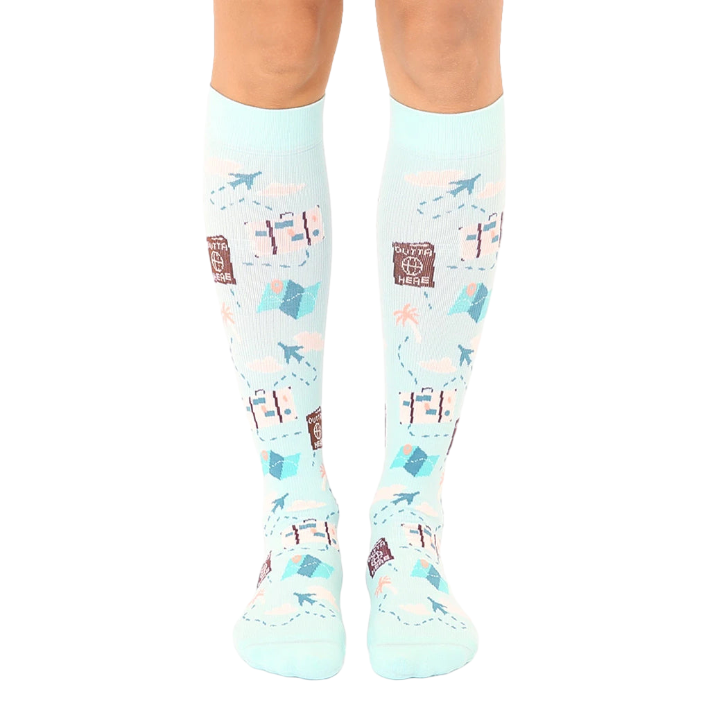 Pair of light blue knee-high socks with a travel theme.  The design includes suitcases, airplanes, maps, and the phrase 'Outta Here'. [lf]