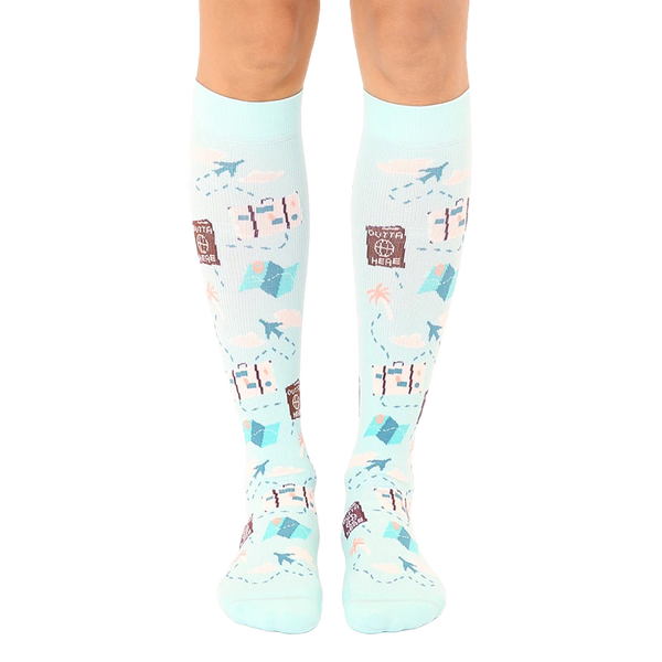 Pair of light blue knee-high socks with a travel theme.  The design includes suitcases, airplanes, maps, and the phrase 'Outta Here'. [lf]