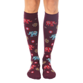 Pair of women's burgundy knee-high socks with colorful elephant and sun designs. [lf]