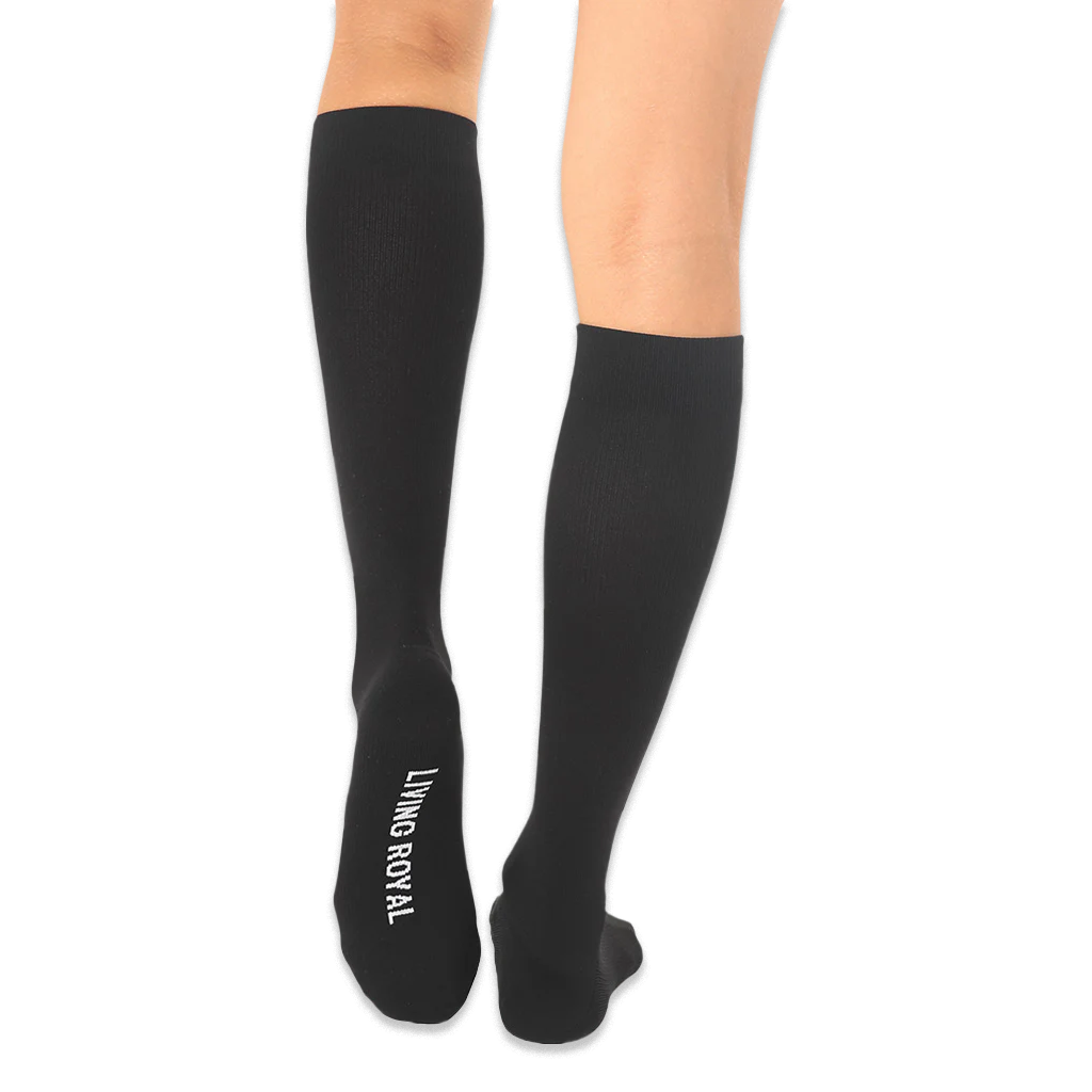 Back view of solid black knee-high socks with the words LIVING ROYAL printed in white on the bottom of the left foot.