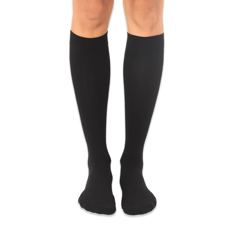 Solid black knee-high socks worn on a person's legs against a dark background, showing a smooth knit texture.