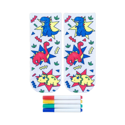 Pair of white ankle socks featuring colorful cartoon dinosaurs and geometric shapes. Includes four fabric markers for coloring.