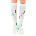 A pair of cream-colored knee-high socks adorned with a repeating pattern of teal and green cacti. [lf]