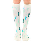 A pair of cream-colored knee-high socks adorned with a repeating pattern of teal and green cacti. [lf]